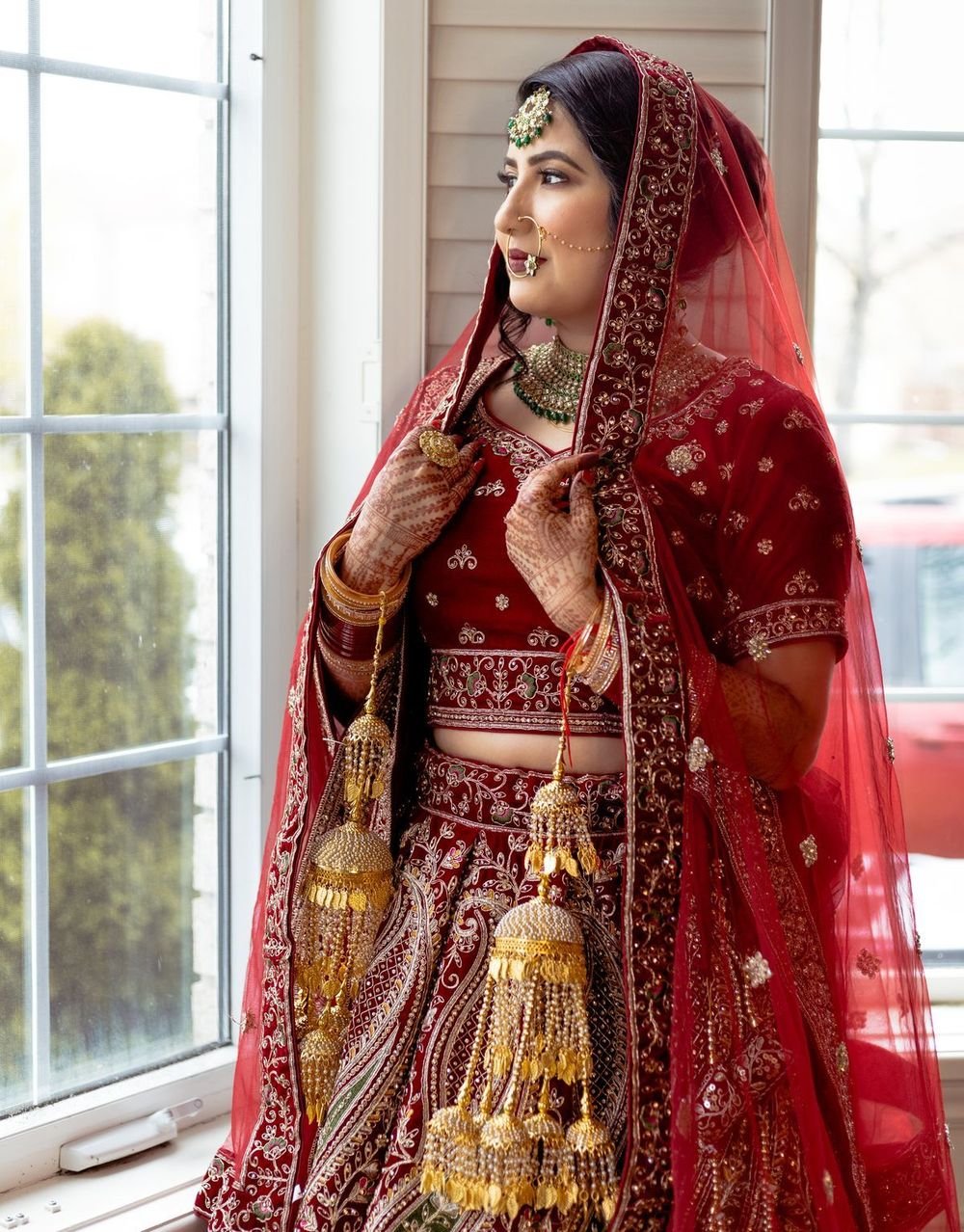 Bride in a red lehenga by a window