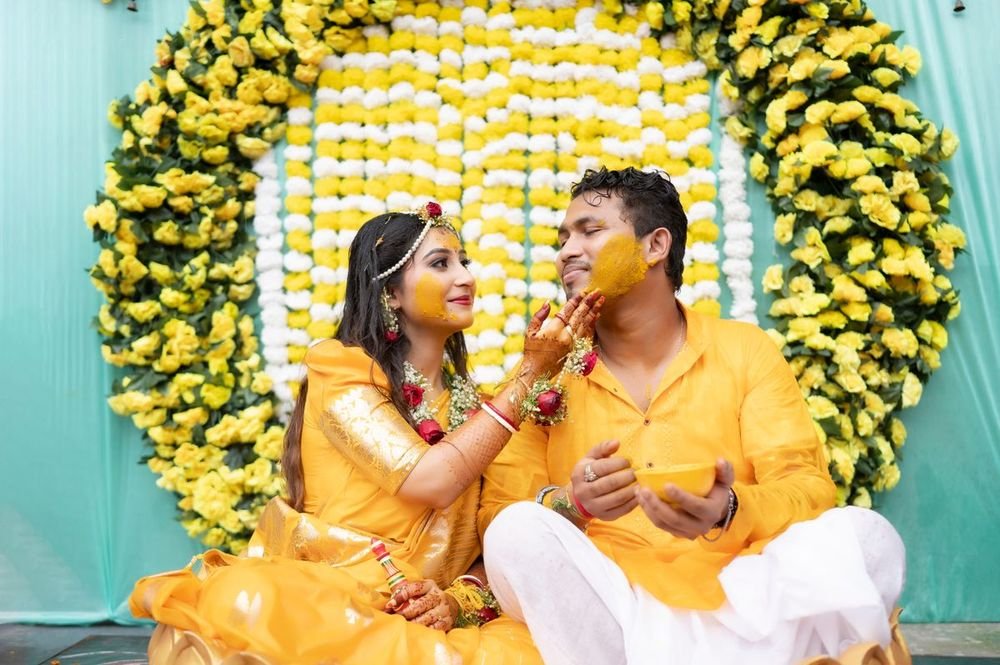Couple at their haldi in front of a marigold wall
