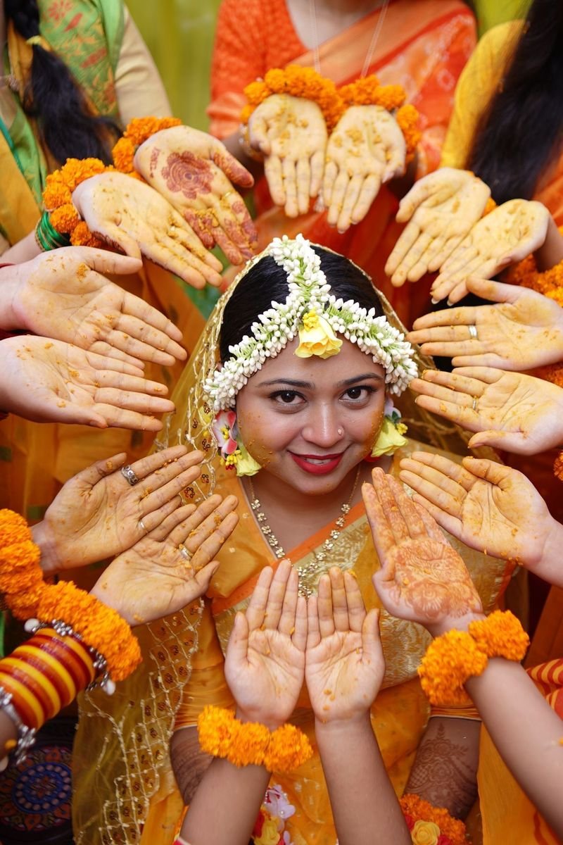Bride at her haldi, framed by hands dipped in turmeric