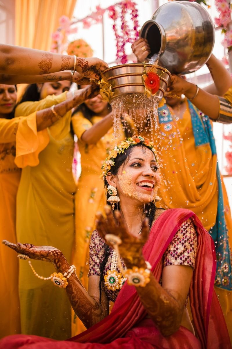 Bride laughing as turmeric water is poured at her haldi